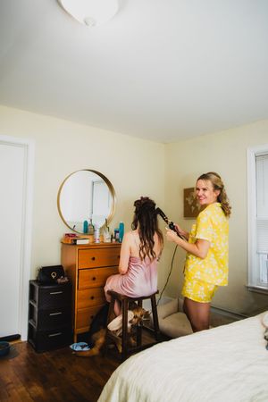People getting ready in a bright bedroom with wooden furniture and white walls.