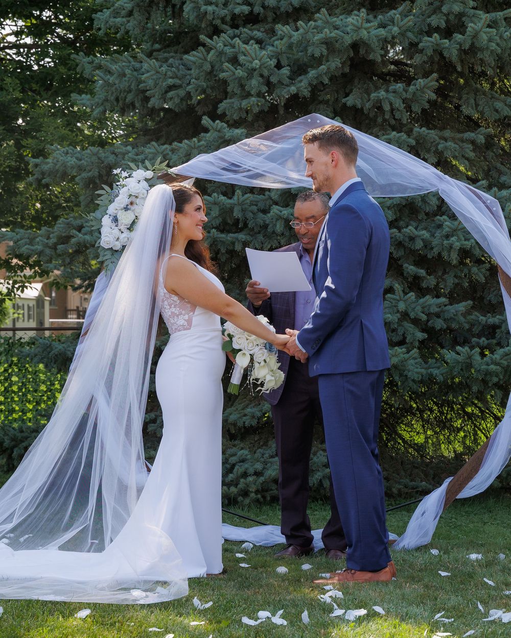 A couple shares a joyful moment during their outdoor wedding ceremony as the bride's veil flows in the breeze.