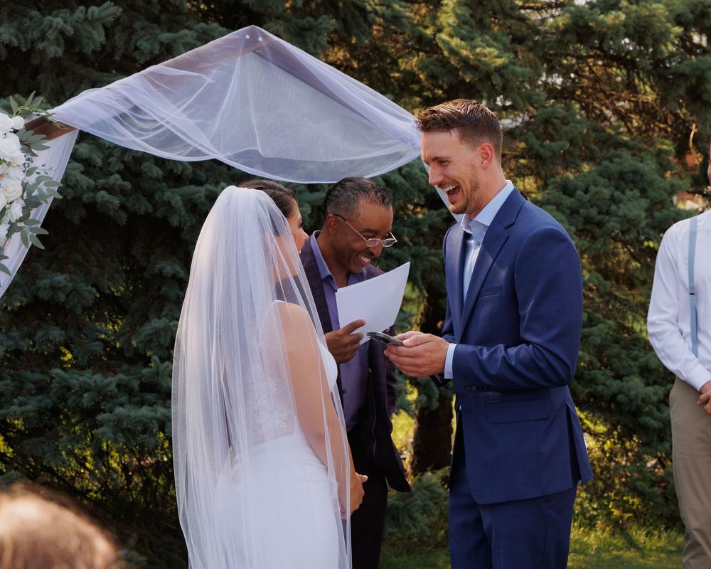 A couple shares an intimate moment during their outdoor wedding ceremony as sunlight filters through trees in the background.