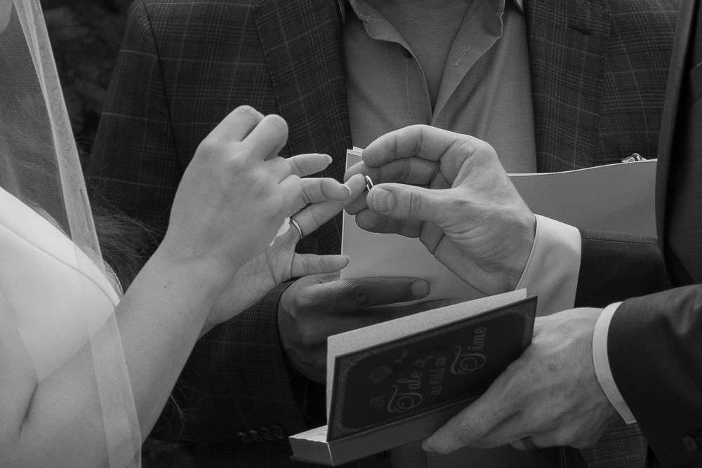 Close-up black and white photo of hands exchanging wedding rings during a marriage ceremony.