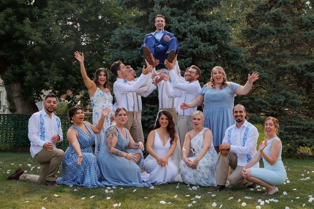 Group in matching light blue outfits sitting and laughing together during outdoor photo session in park setting.