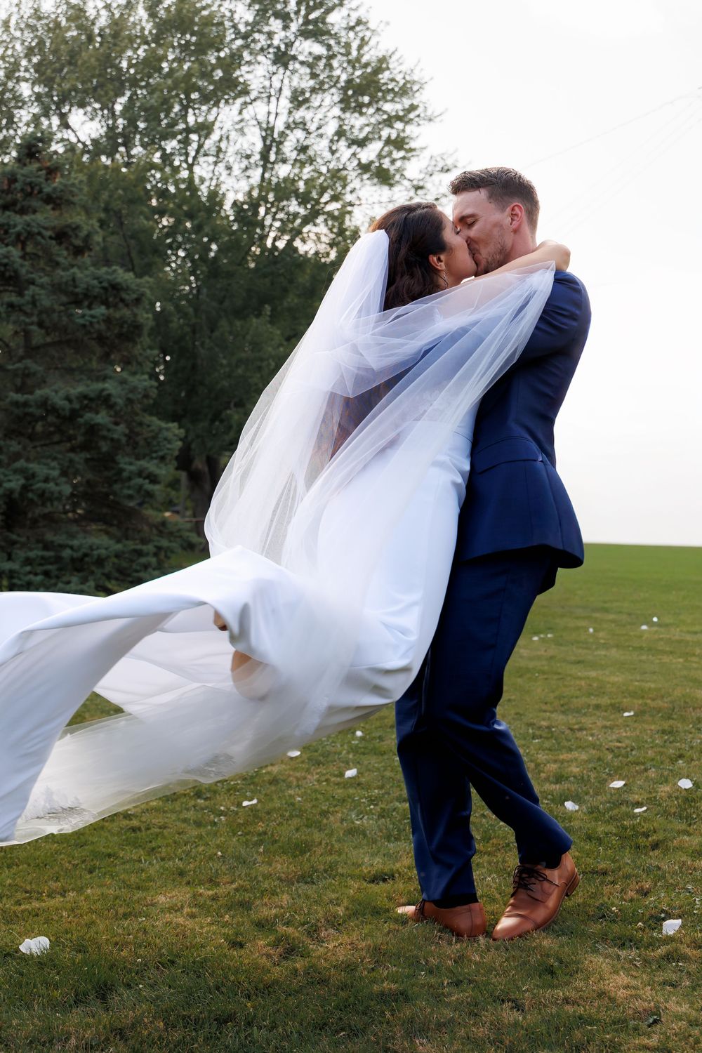 A couple in wedding attire dances and spins on a grassy field with flowing white veil creating romantic movement.