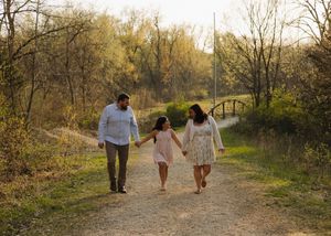 Happy family of three walking hand-in-hand on a scenic nature trail at golden hour.