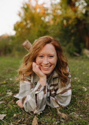 Smiling redhead woman lying on grass in autumn park wearing plaid flannel shirt.