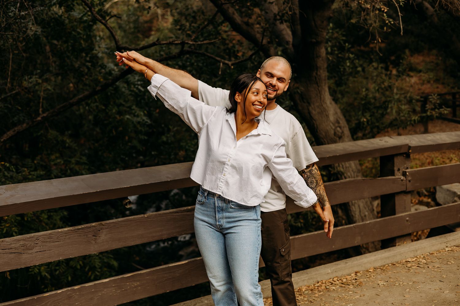 Newlyweds walking hand in hand on a paved path through wooded area.