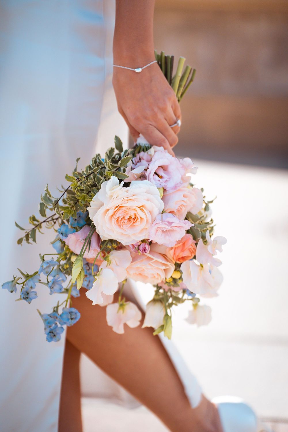 Delicate bouquet of pink roses and blue flowers held against a white dress.