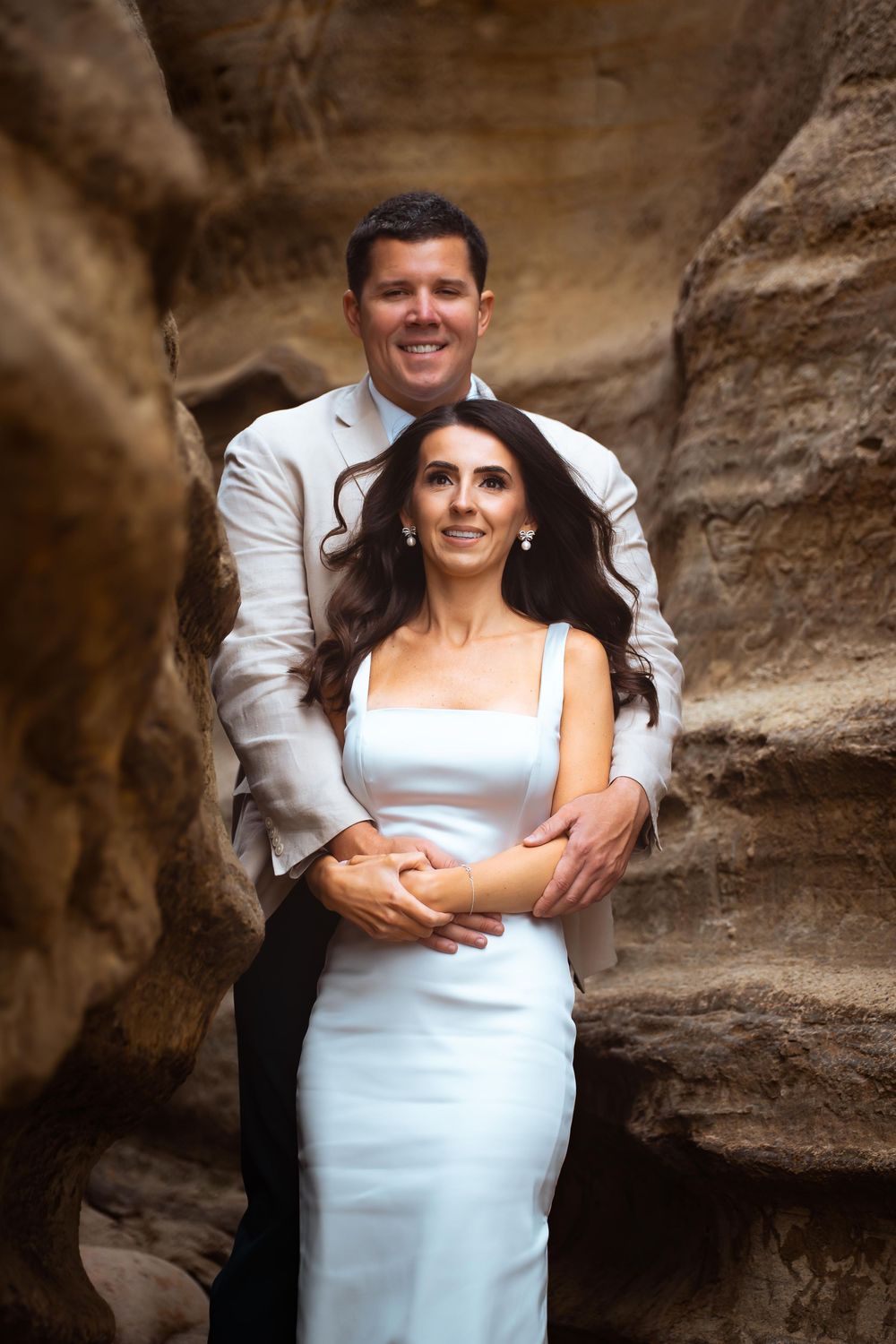 Romantic couple pose against textured rock formations in formal attire.