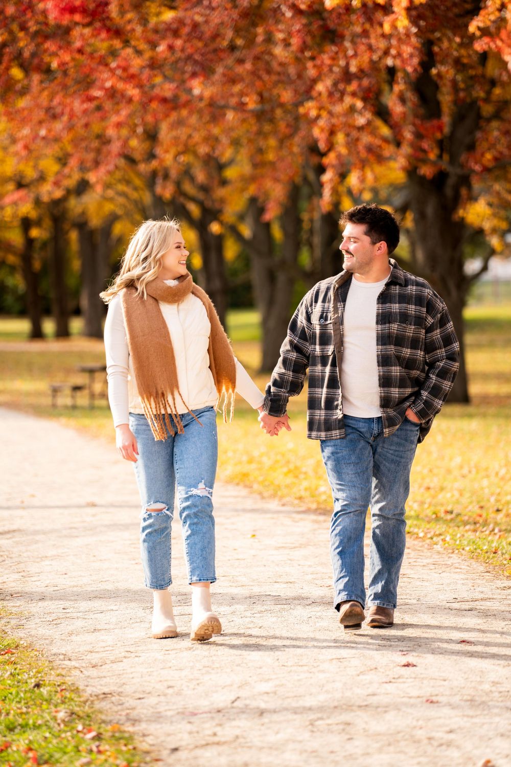 A couple walks hand in hand down a leaf-covered path in autumn.