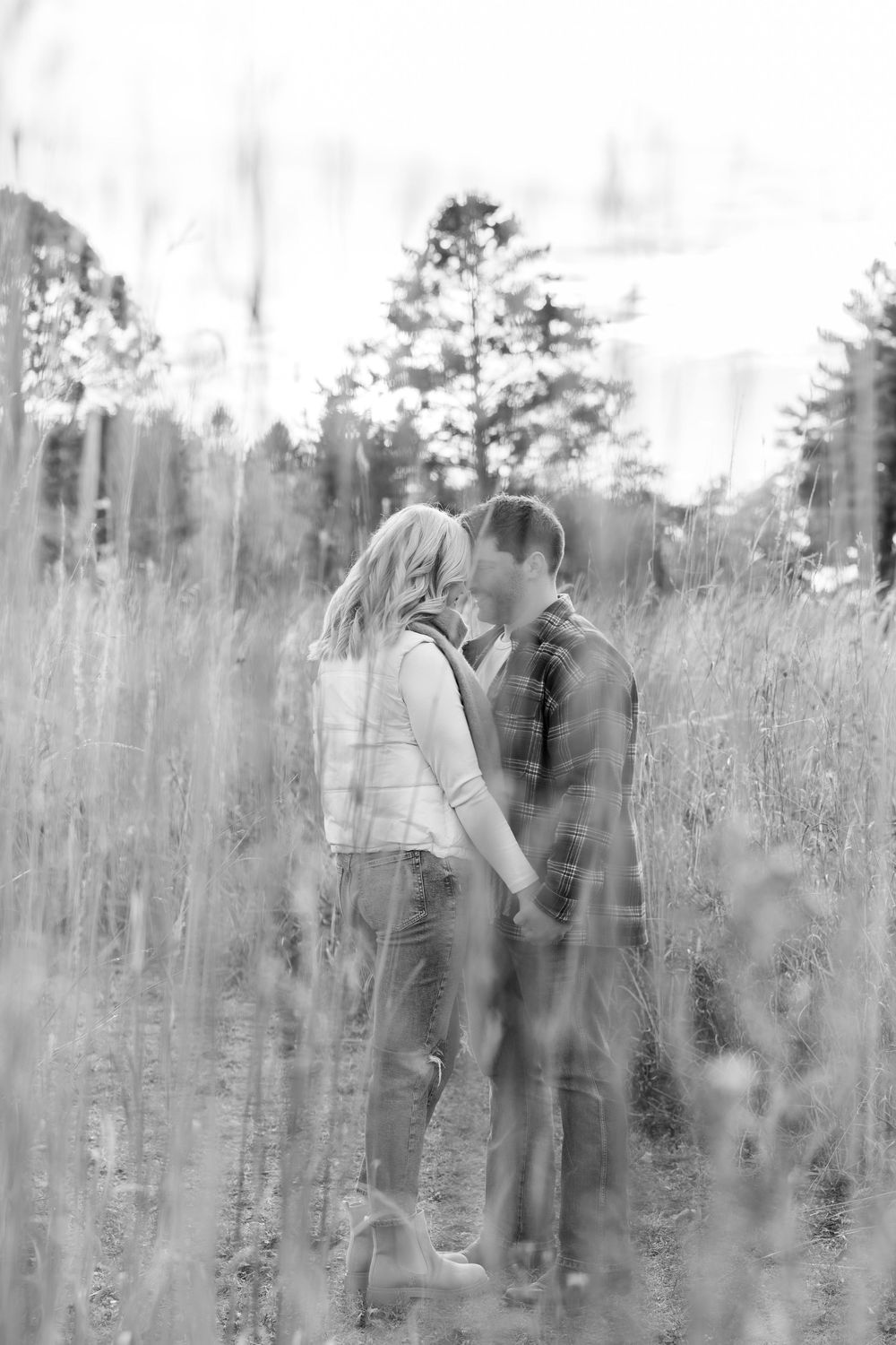A black and white photo of a couple embracing in tall grass.