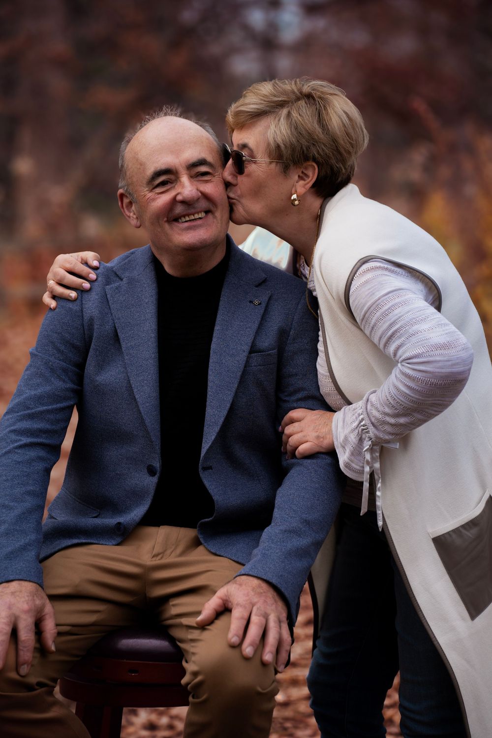 A couple shares a tender moment on a bench in autumn.