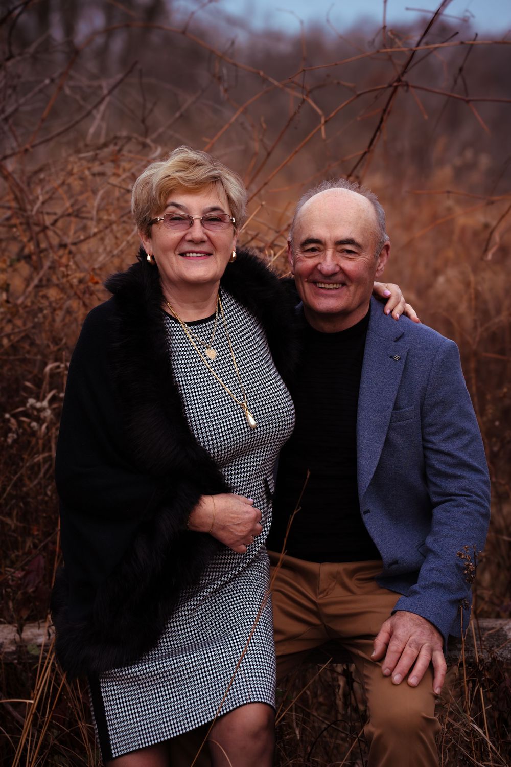 Couple sitting together outdoors during autumn with brown foliage in background.