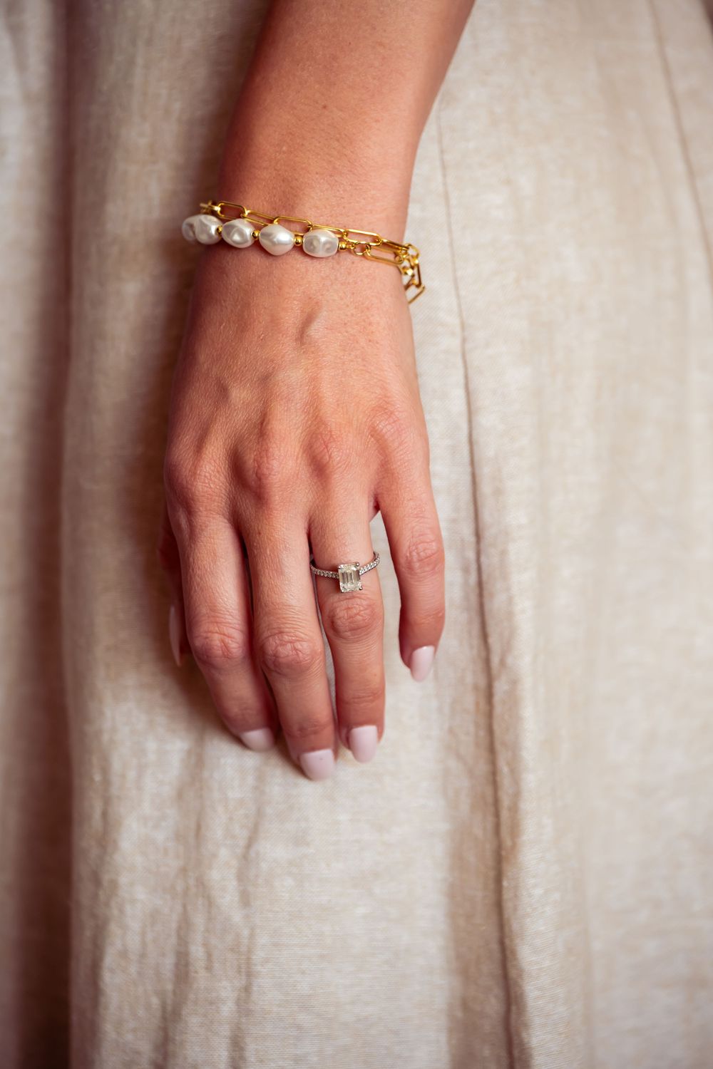 Close-up of hands wearing elegant jewelry and rings against a light fabric background.