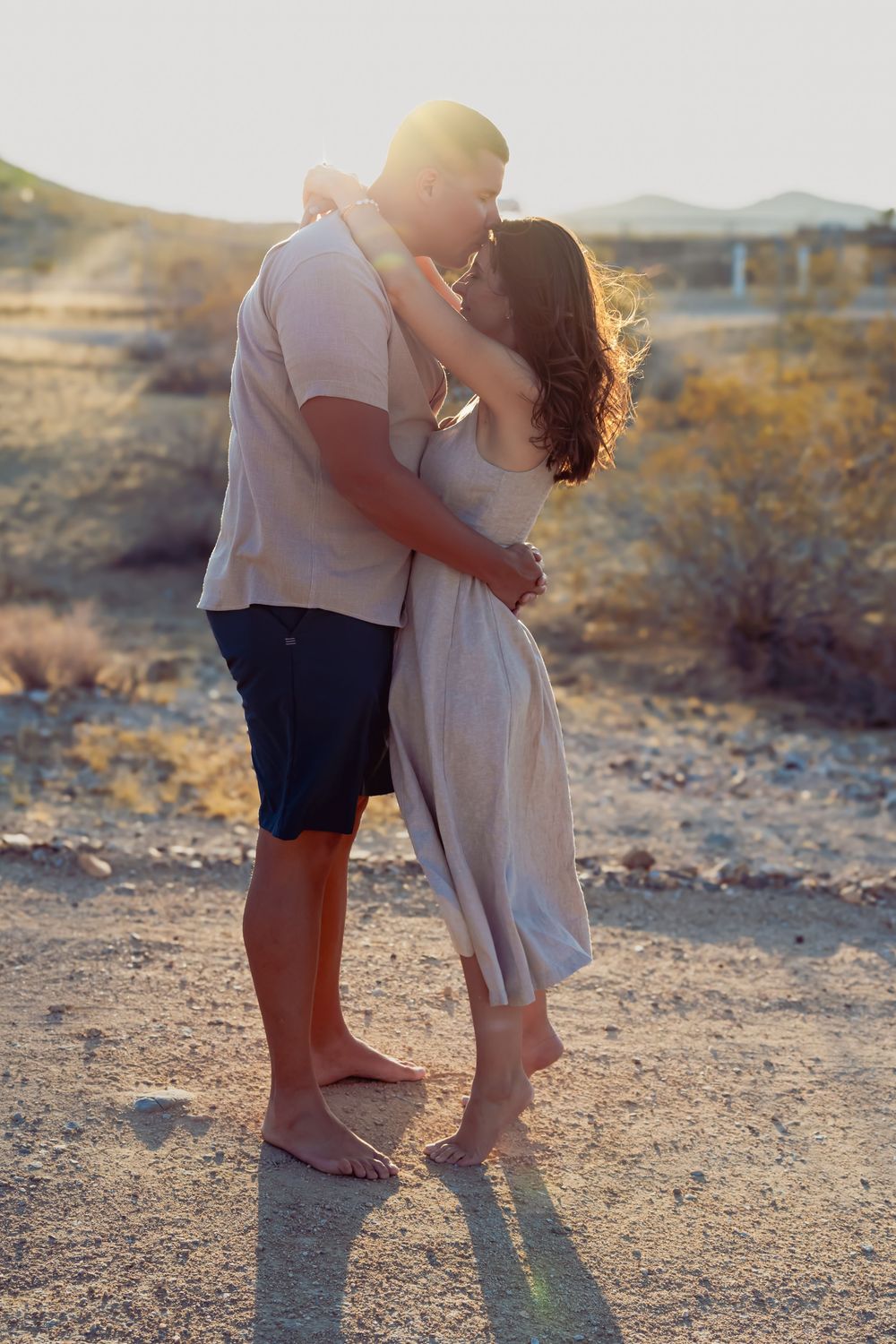 Couple embracing on sandy desert terrain during sunset.