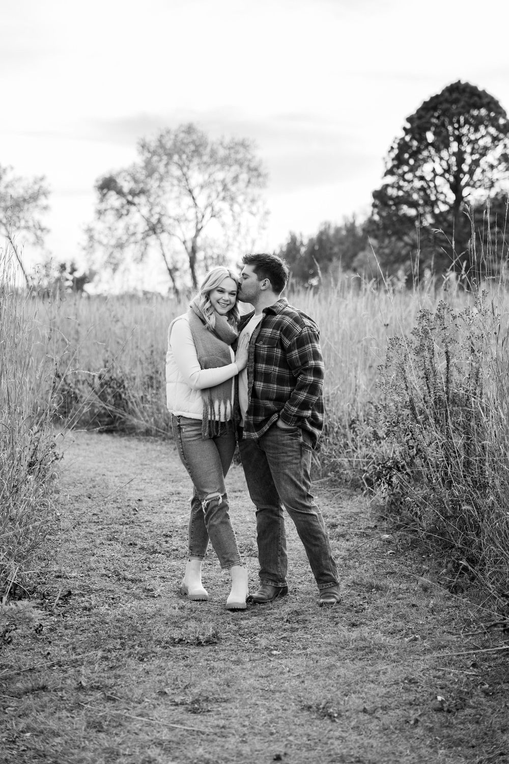 A couple embraces on a rustic path surrounded by tall grass.