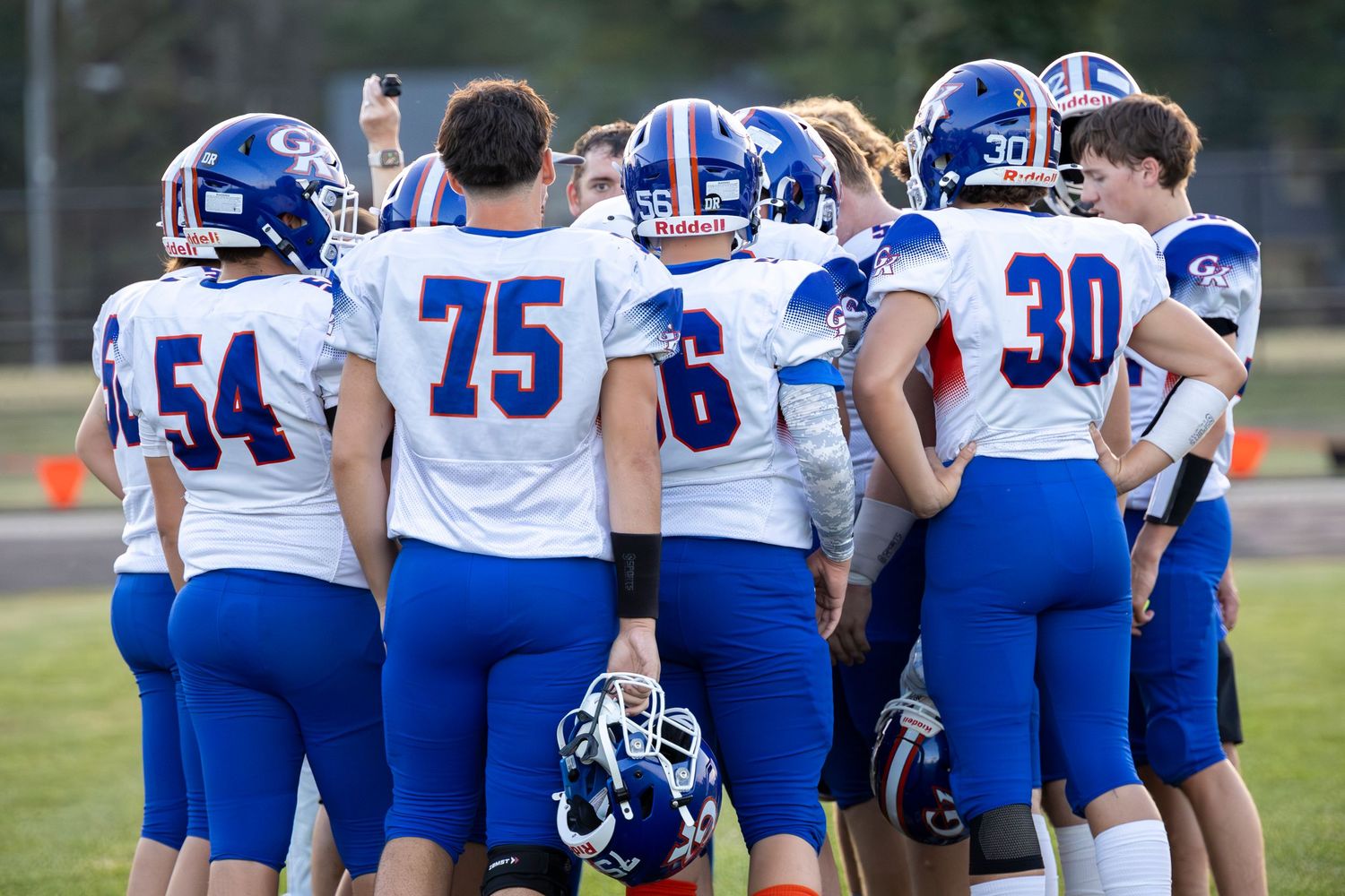 Football players in blue and white uniforms huddle during a game.