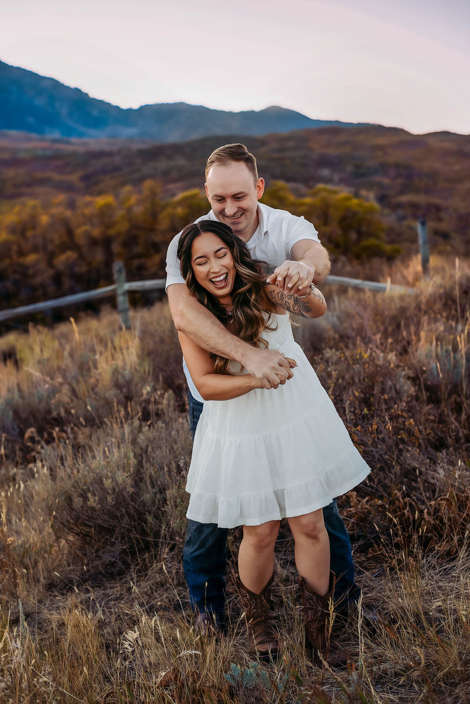 Couple laughing and hugging at engagement session with fall foilage in the back