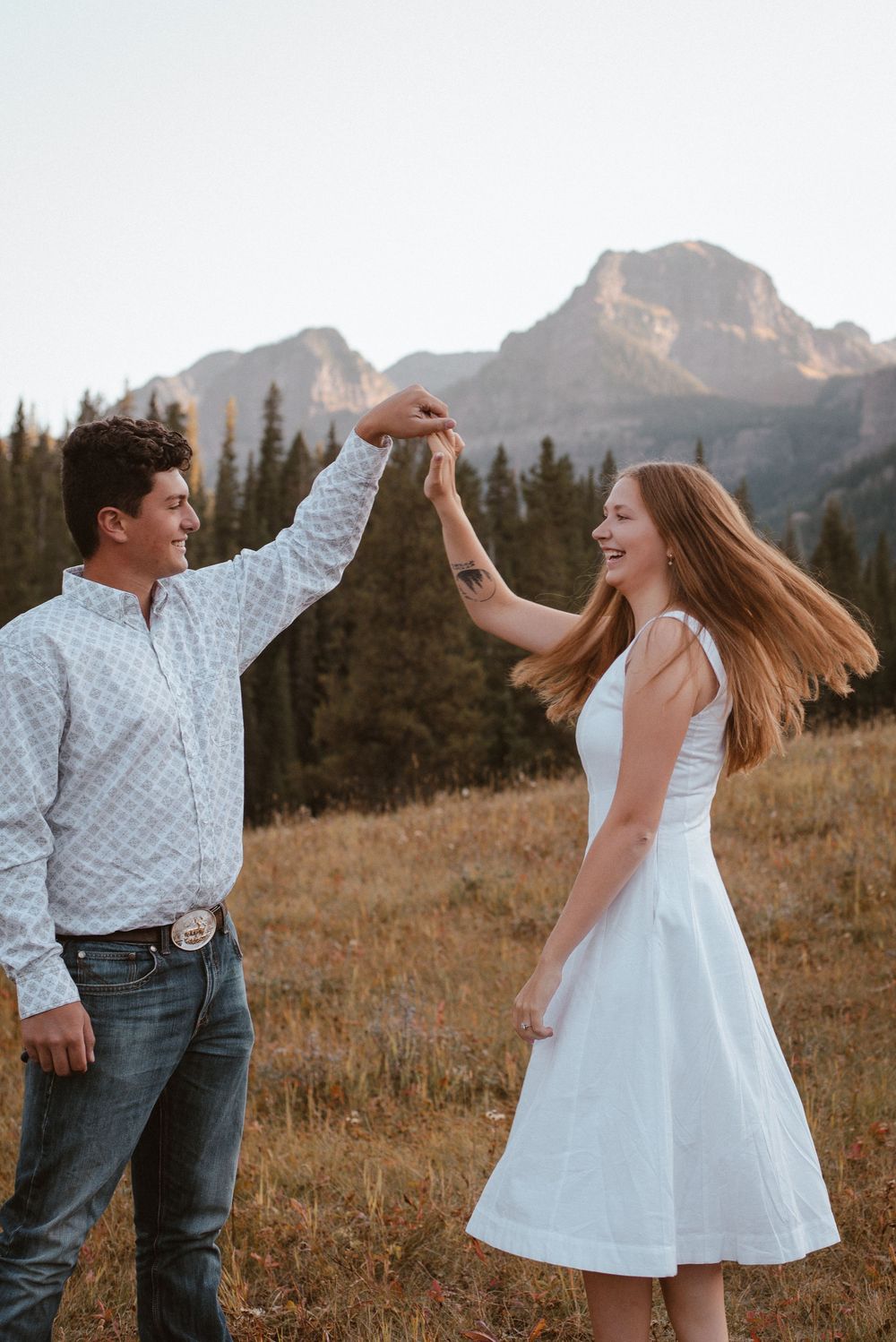 A couple dances and twirls in a mountain meadow during golden hour.