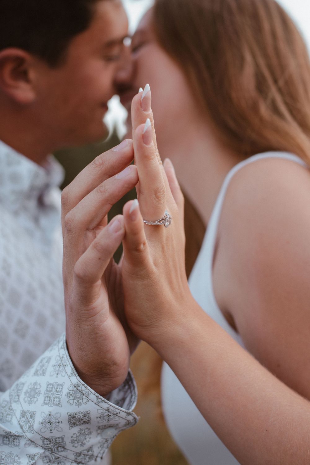 Close-up of hands touching with an engagement ring visible against white clothing.
