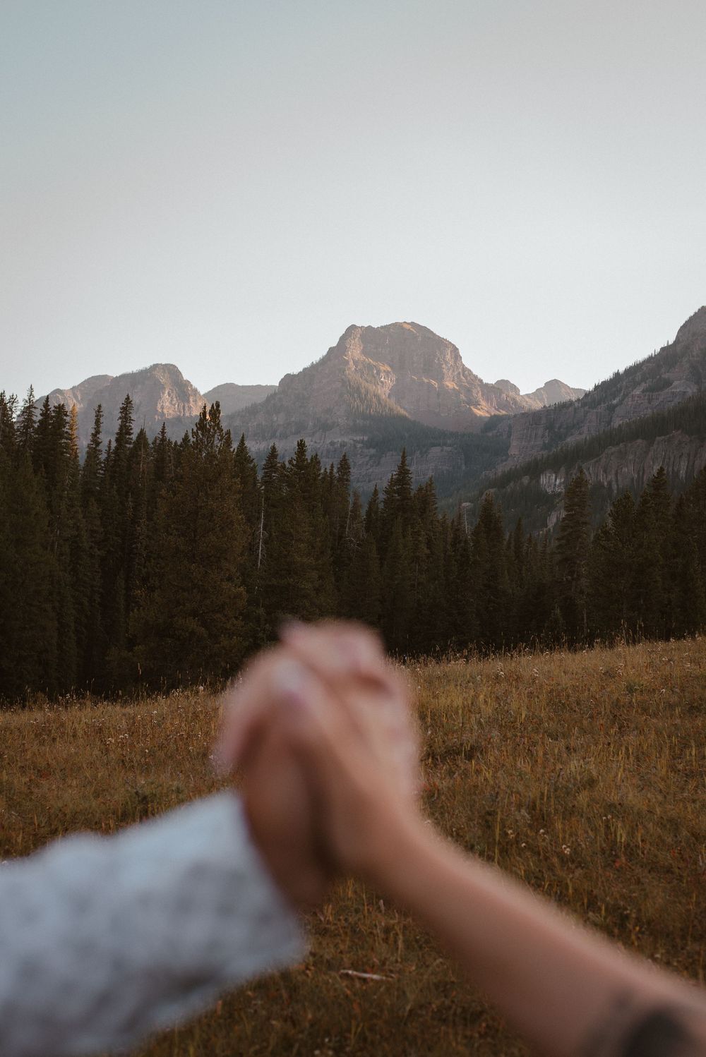 Joined hands frame a stunning mountain landscape with evergreen forest at sunset.
