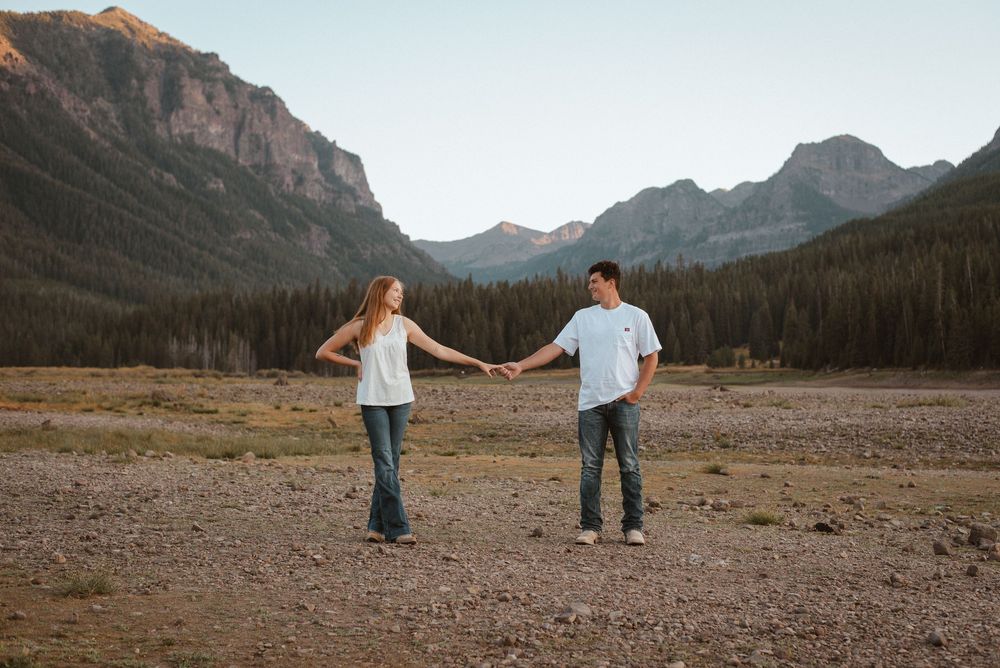 A couple walks together across a rocky mountain landscape with distant peaks.
