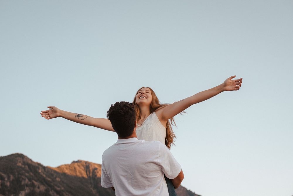Two people spread their arms wide with joy against a mountain backdrop.