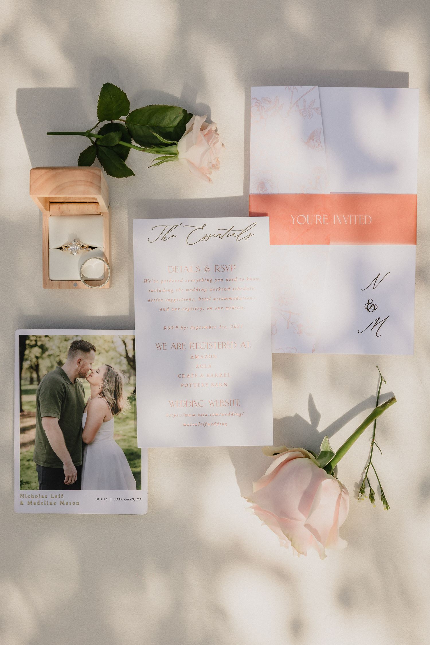 Wedding details flatlay with invitation, rings in peach box, pink roses and delicate stationery on light background.