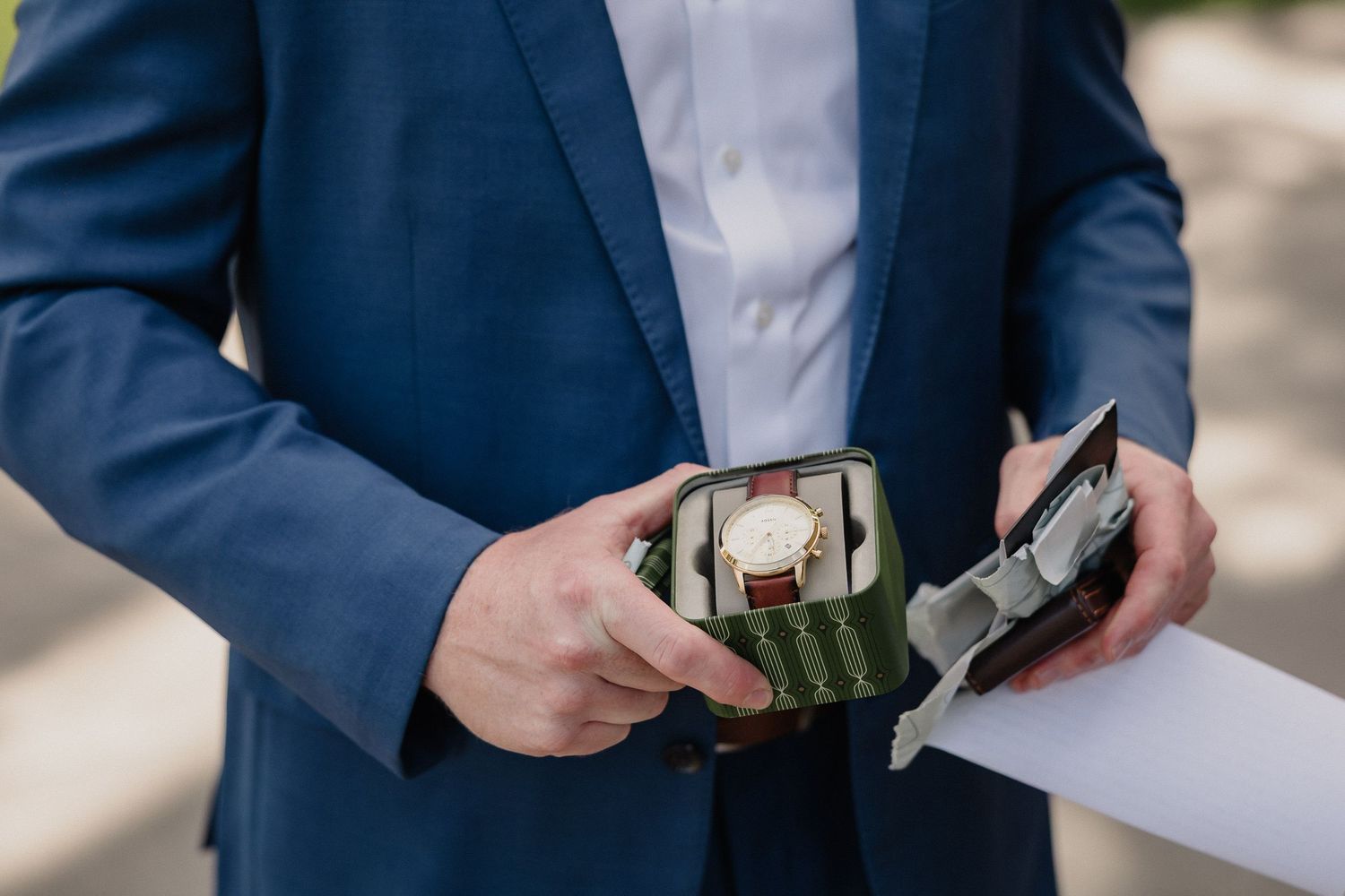 Close-up of hands in navy suit jacket holding papers outdoors.