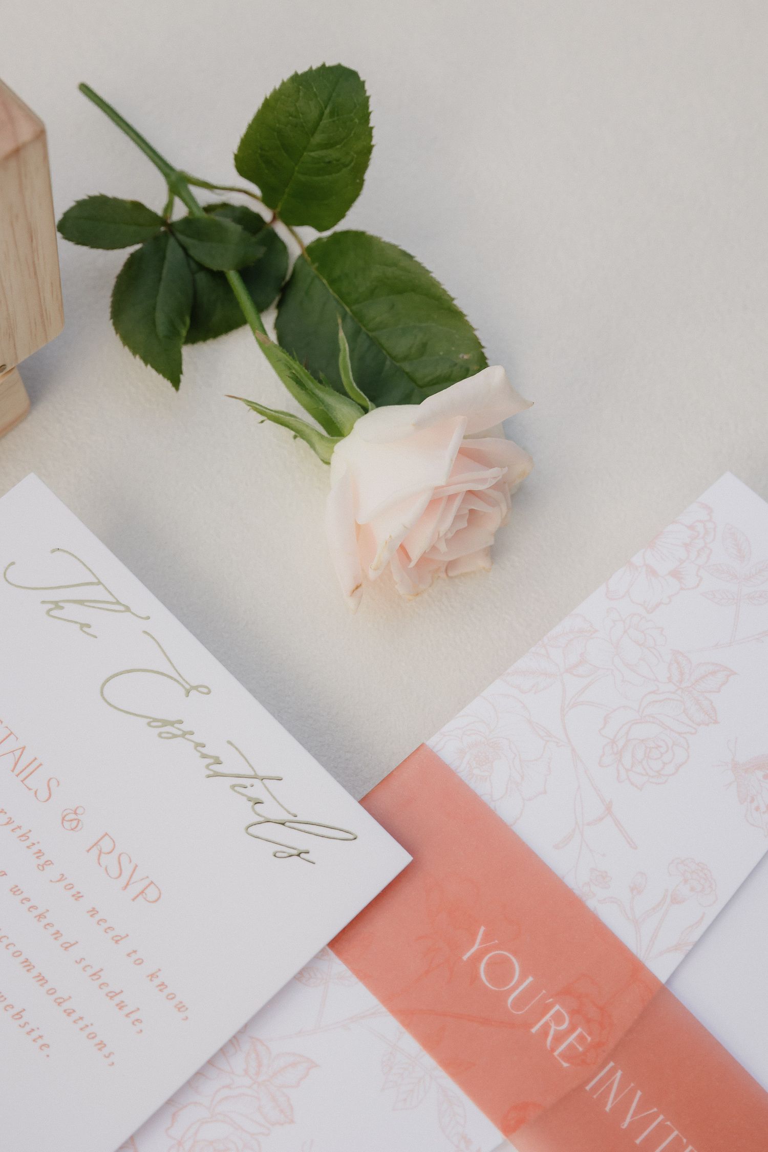 Wedding invitation cards in coral and white with delicate floral designs and elegant calligraphy lay beside a pink rose.