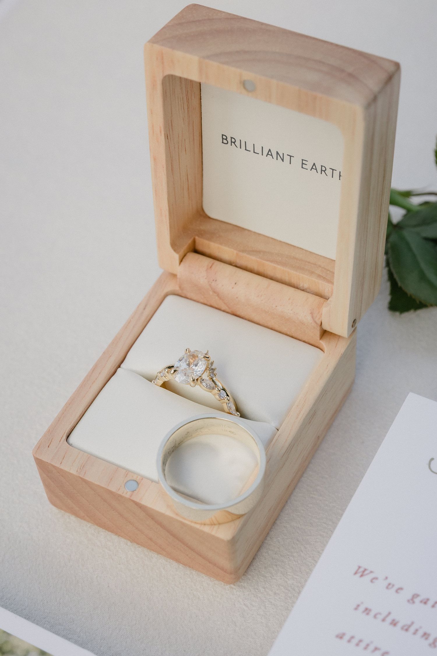 Elegant engagement ring displayed in a light wooden box against a white background.