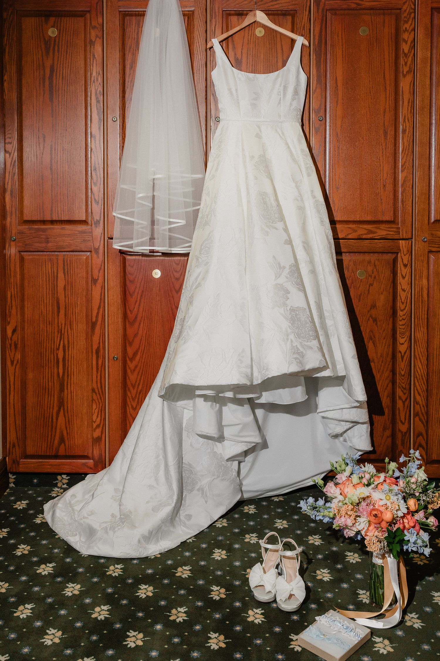 Wedding dress and bridal accessories including white shoes and floral bouquet displayed against wooden paneling.