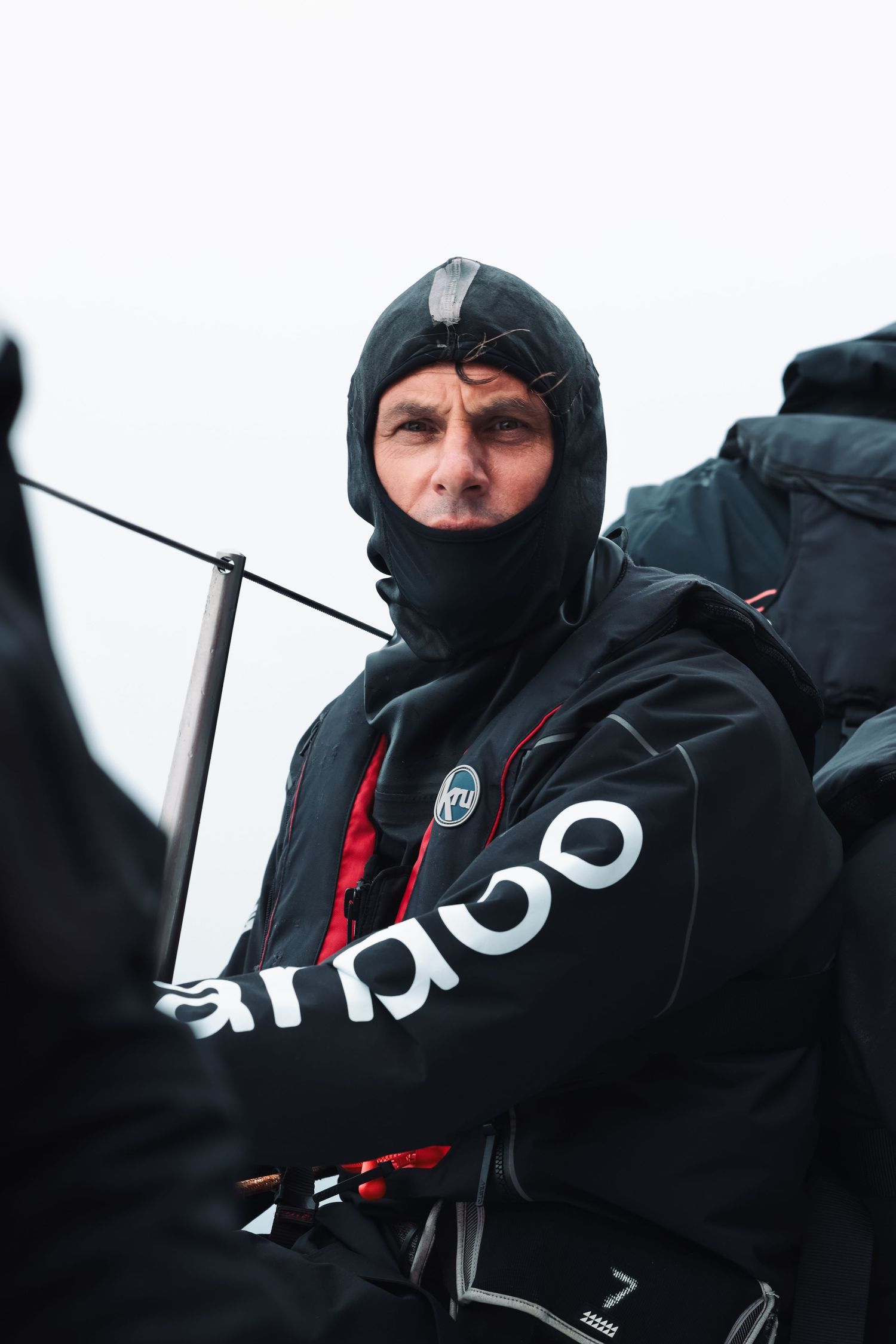 Crew members in black weatherproof gear operating sailing equipment.
