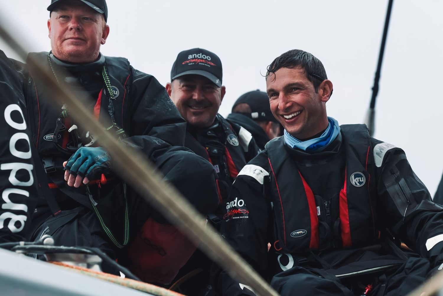 Crew members in matching black jackets working together on sailboat deck.