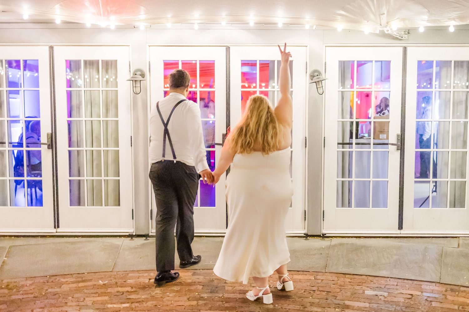String lights illuminate a long white hallway with French doors and pink and blue lighting accents creating an elegant ambiance.