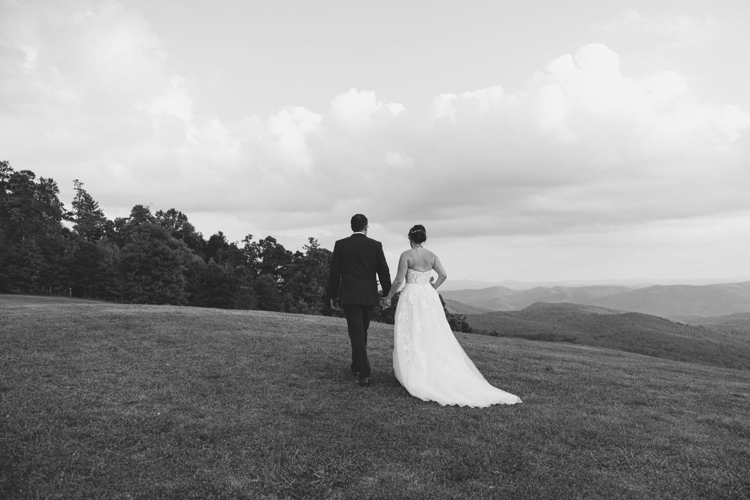 a newly married couple walking in a field with a mountain back drop. East Coast Luxury wedding photographer, Romantic storytelling