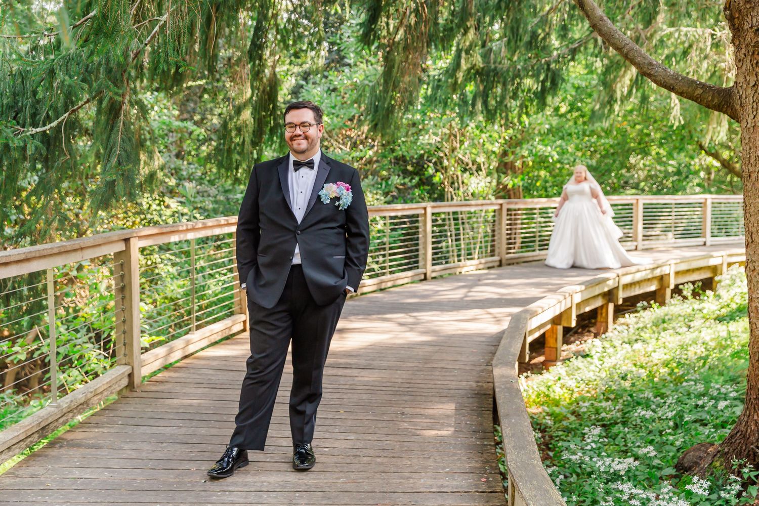 A couple walks along a wooden boardwalk path through a lush green forest setting.