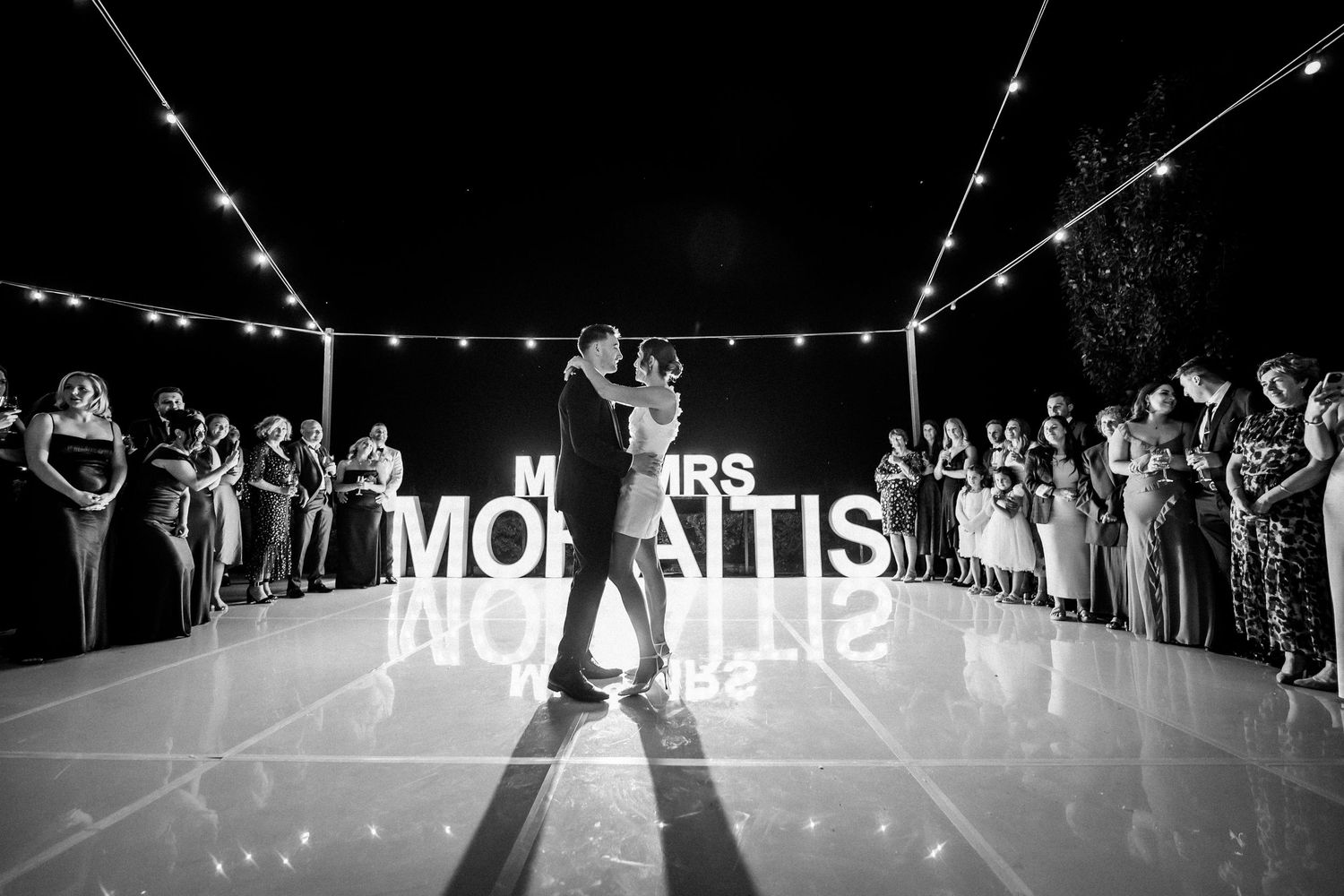 Wedding reception under string lights with illuminated name display.