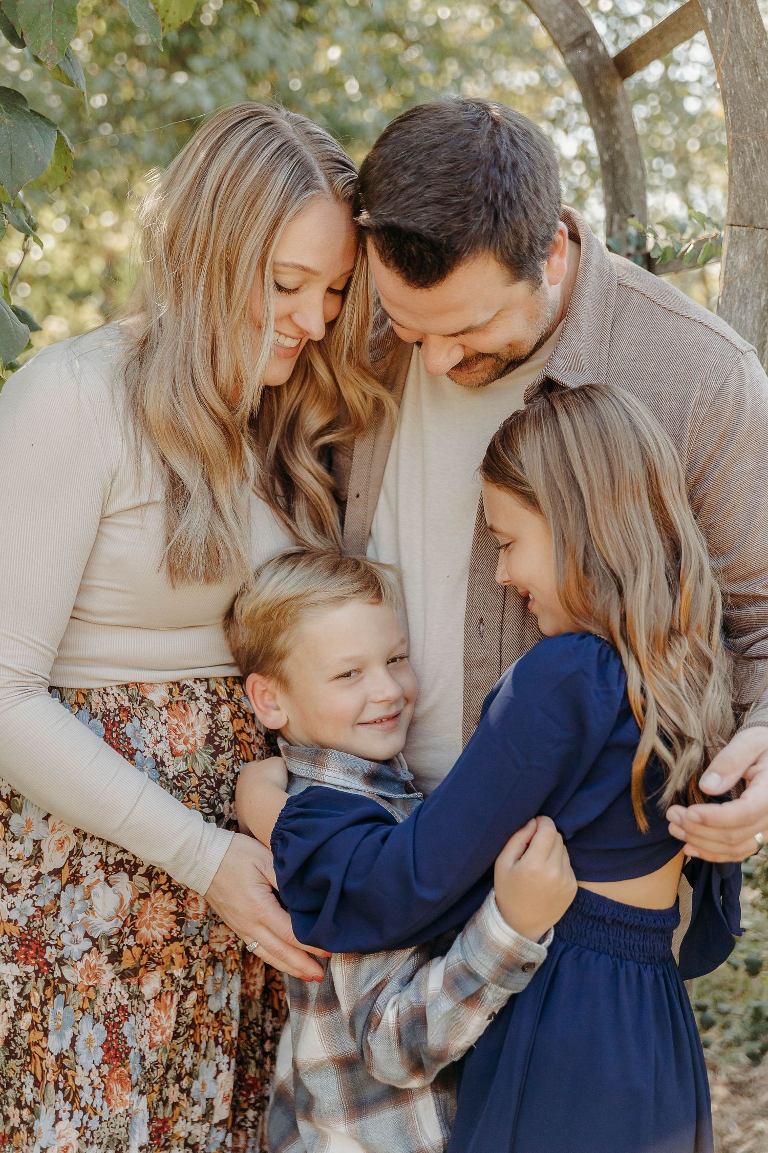 A family shares tender moments together in a series of outdoor portraits with natural lighting and foliage backdrop.