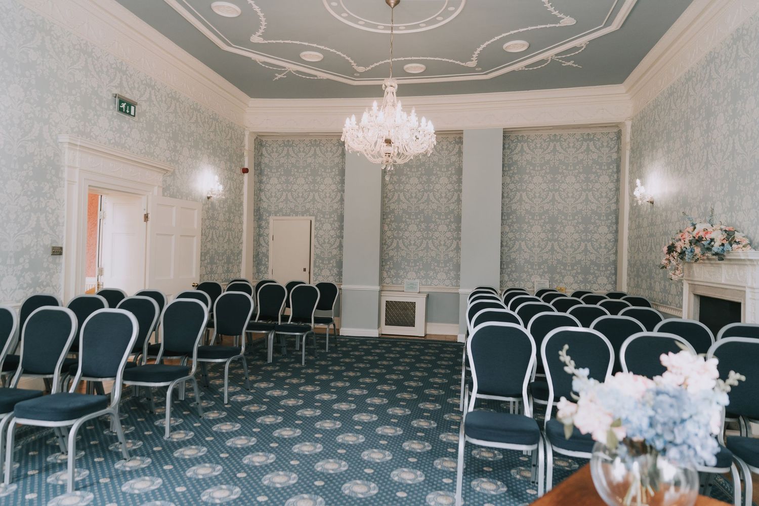 Elegant banquet hall with crystal chandeliers, ornate ceiling details, and rows of black chairs arranged for an event.