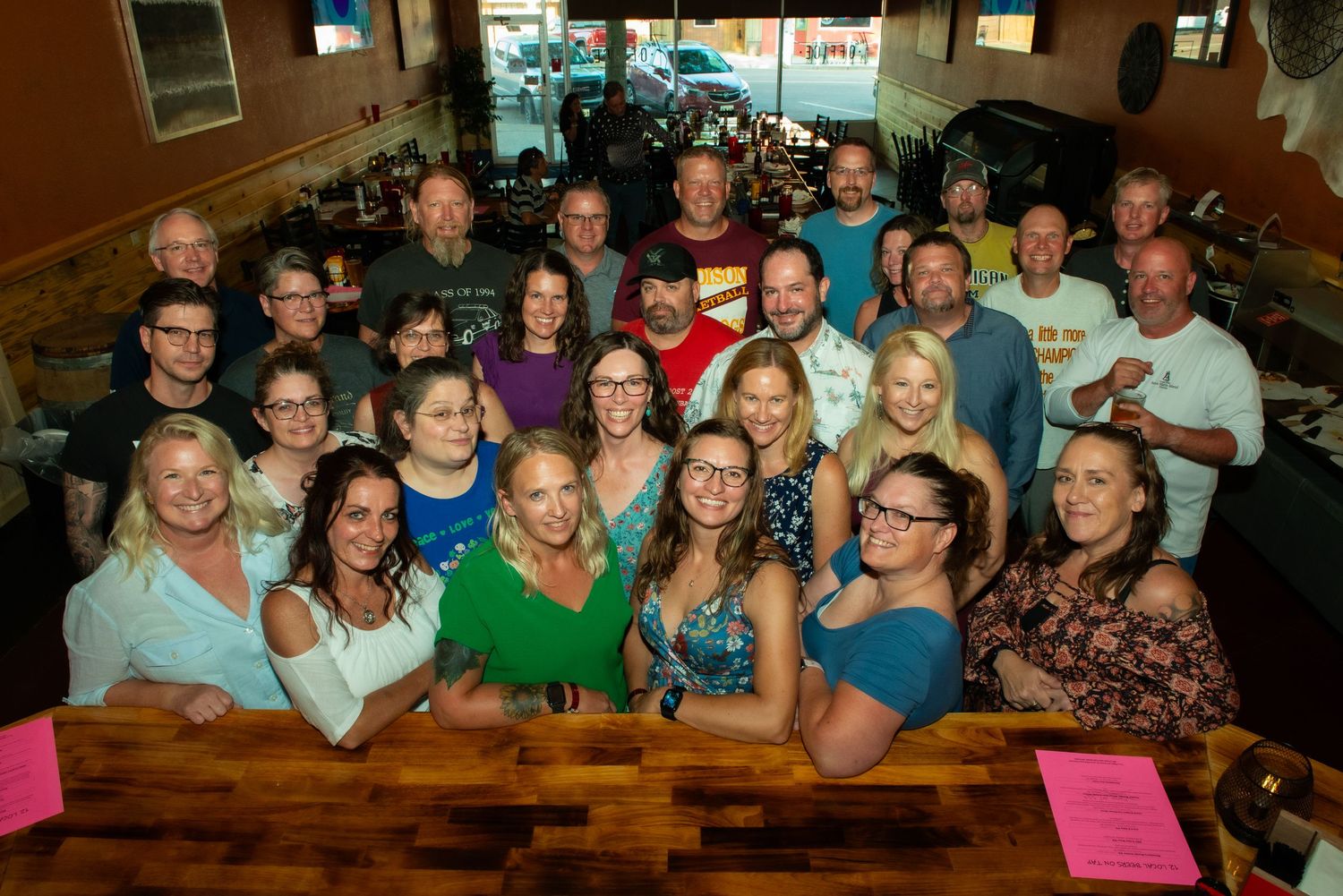 Large group of people smiling together while at restaurant tables for a social gathering.