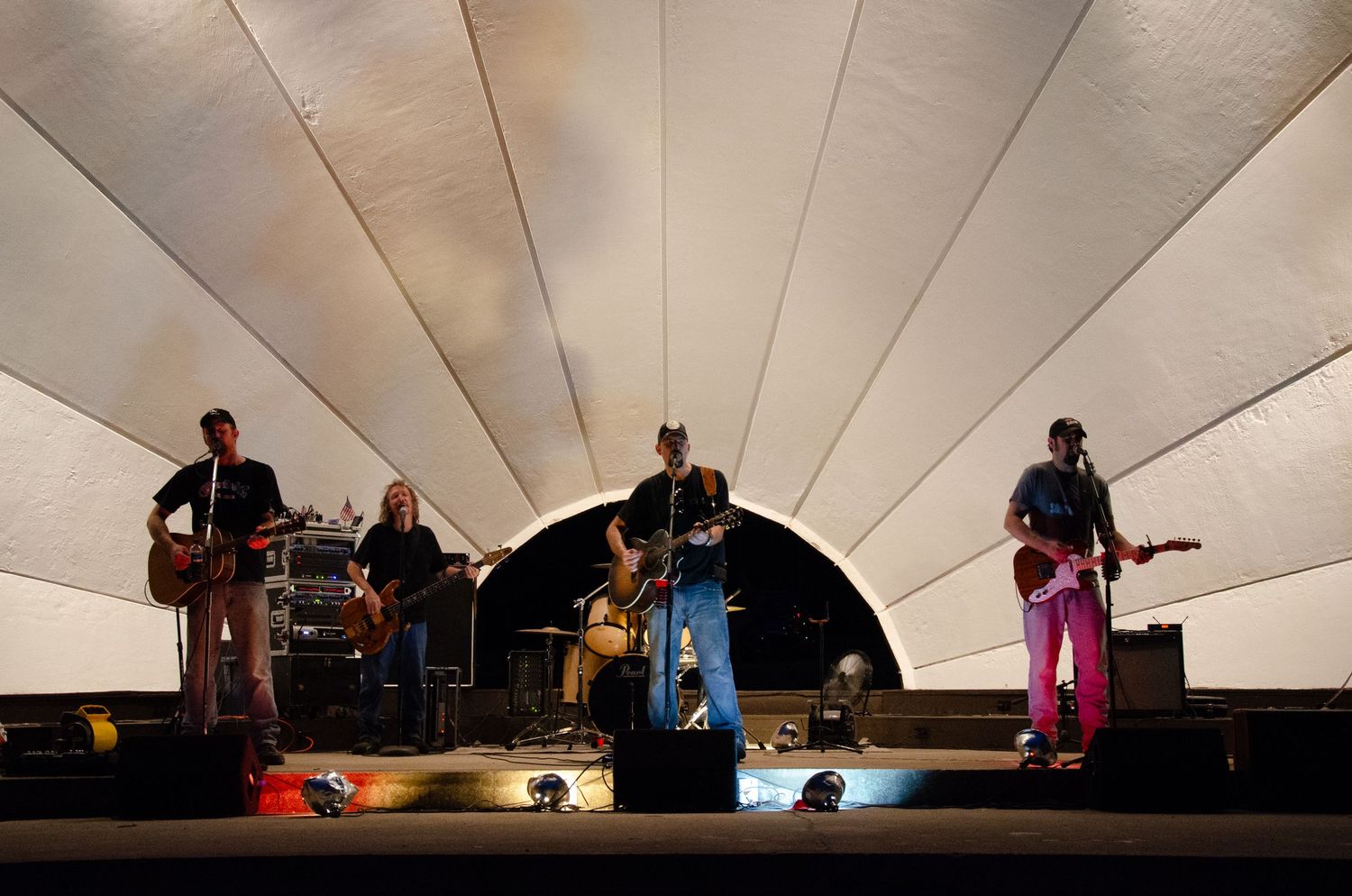 Musicians perform on stage under angular white ceiling panels with dramatic lighting effects during a live concert.
