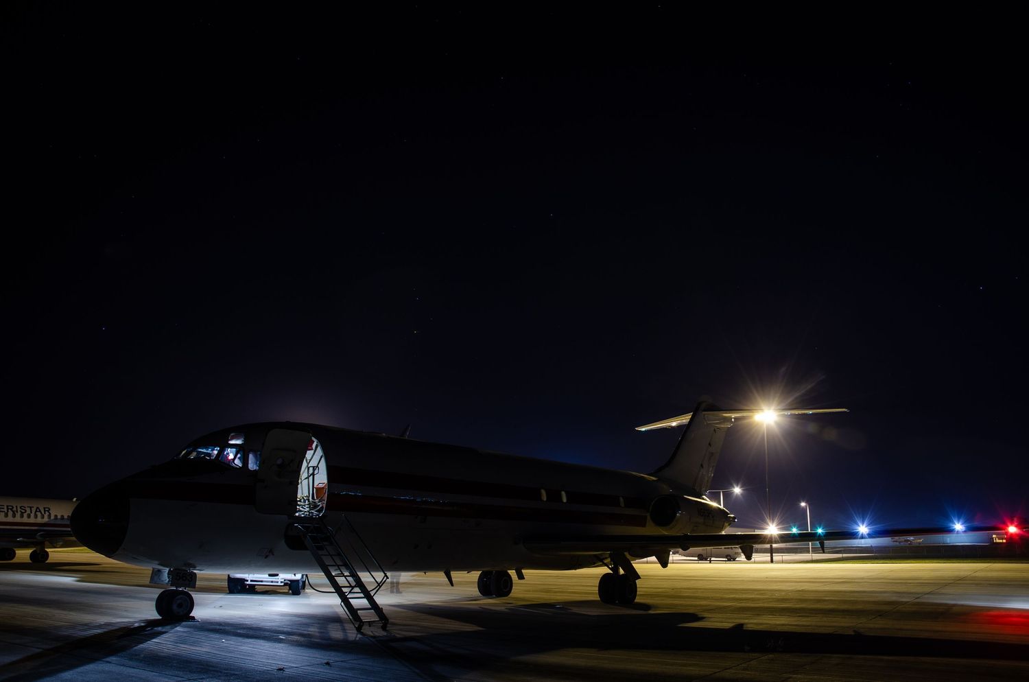 Cargo aircraft silhouetted against dark sky with runway lights illuminating the tarmac at night.