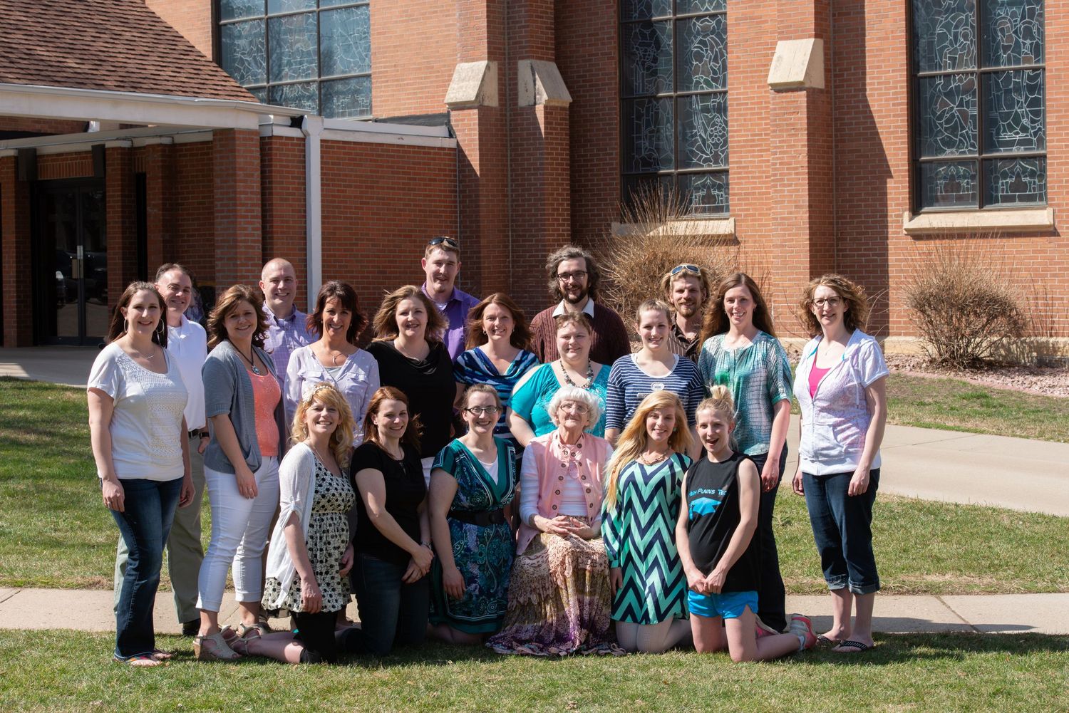 Group of people gathered outdoors in front of a brick building on a sunny day.
