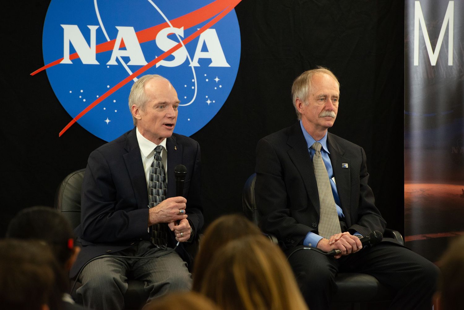 NASA officials sit at a panel discussion table with the agency's logo visible in the background.
