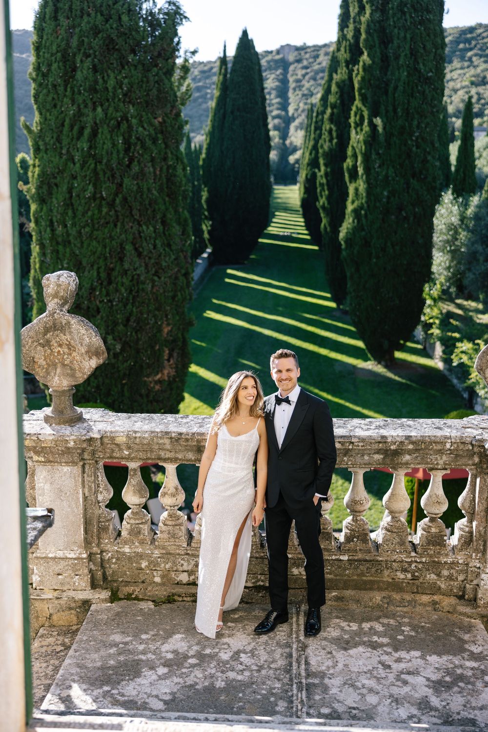 A formal couple posing on a balcony with Italian cypress trees and mountain views.