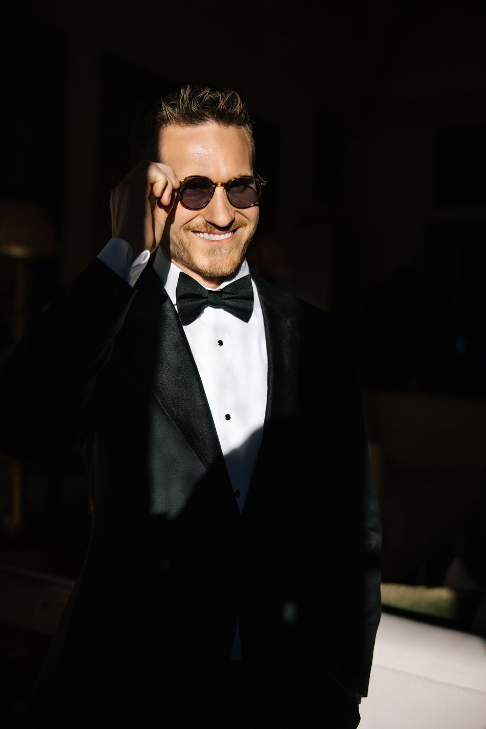 Formal evening attire with black tuxedo, bow tie and sunglasses in dramatic lighting.