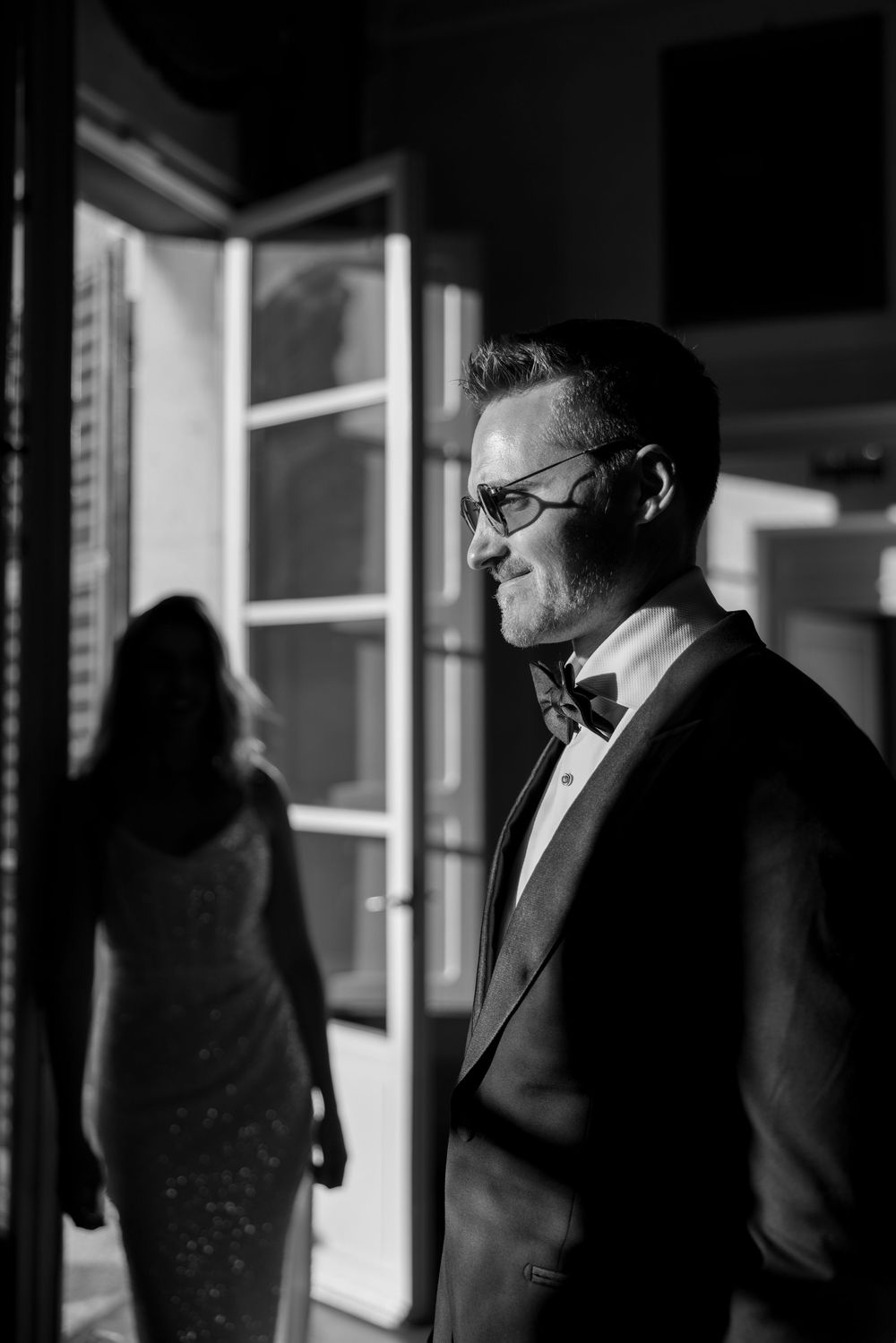 Black and white portrait of men in suits standing near windows in a dark room.