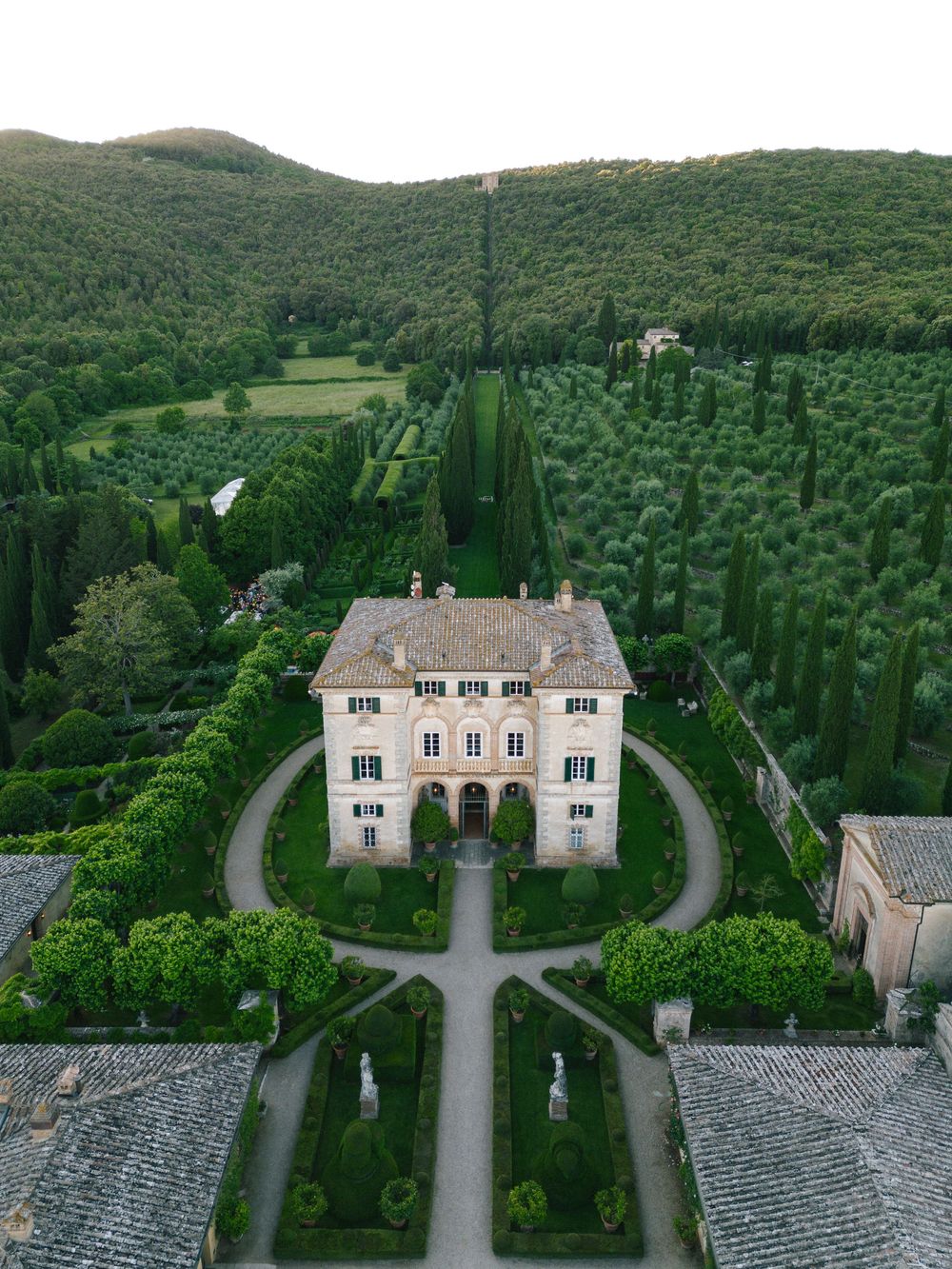 Aerial view of an elegant villa with cypress trees and manicured gardens in Tuscany, Italy seen from multiple angles.