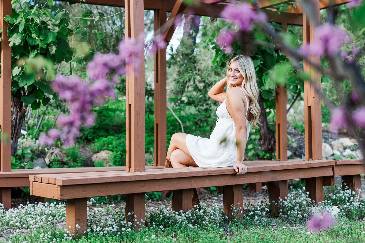 A wooden deck with pink flowering plants creates a tranquil outdoor living space surrounded by lush greenery.