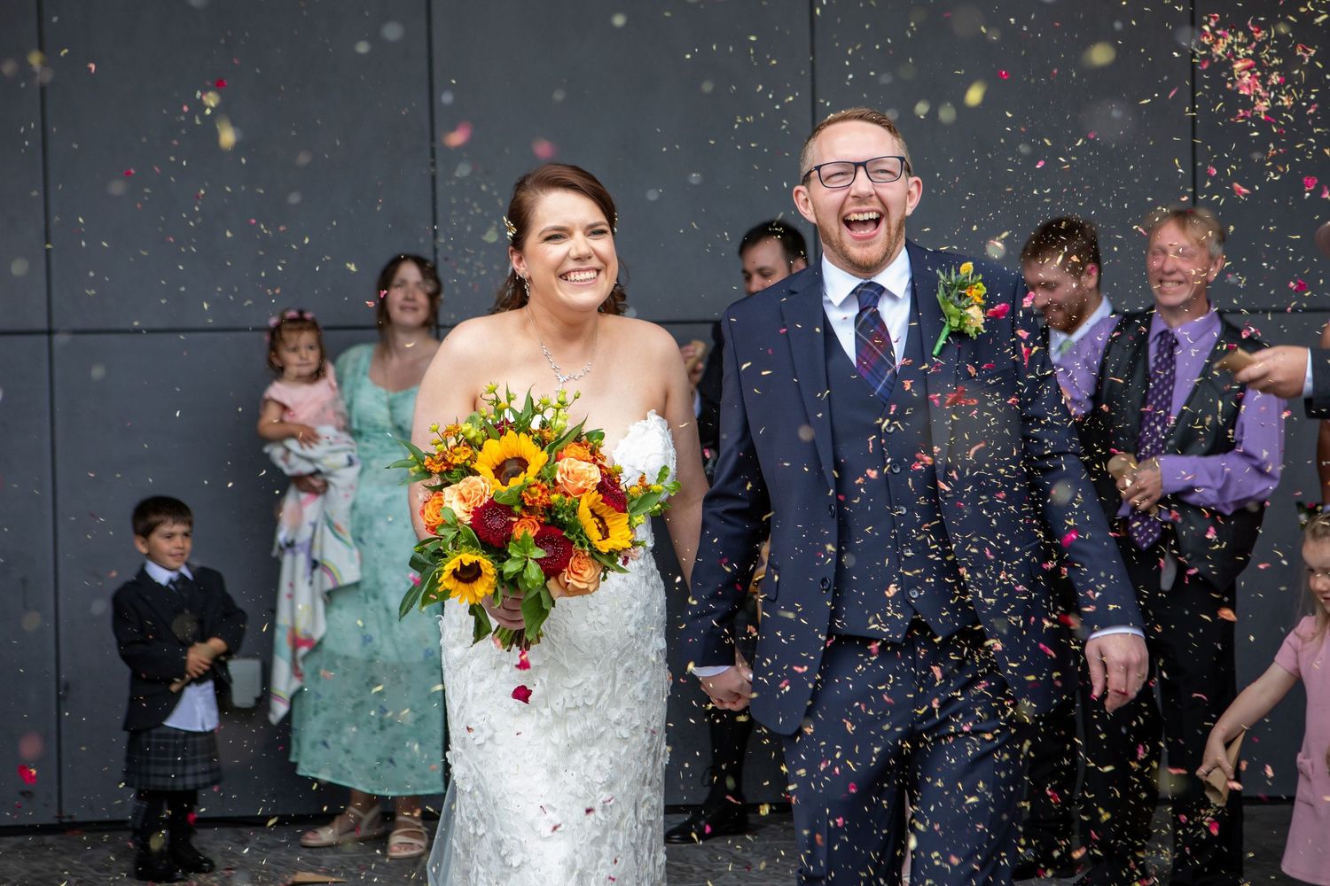 Wedding party celebrates with confetti and sunflowers during outdoor ceremony at dusk.