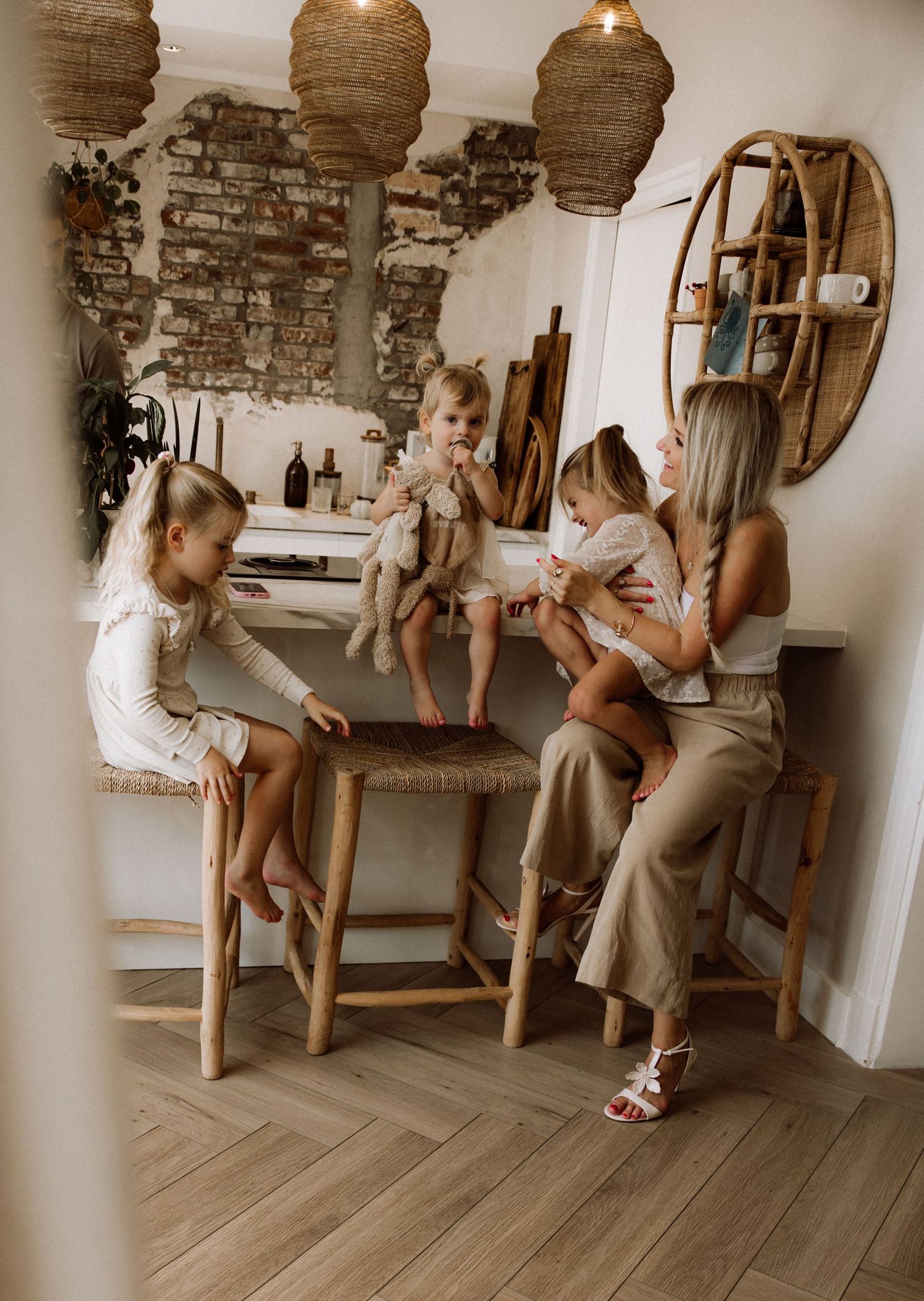 Family gathering around rustic kitchen counter with exposed brick wall and woven pendant lights.